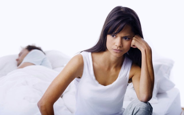 Frustrated girlfriend Frustrated woman sitting at edge of bed while her boyfriend sleeps