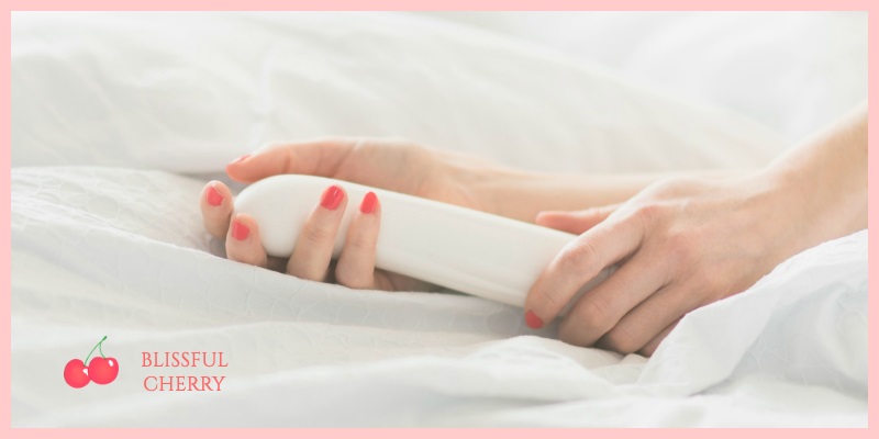 Sex Toy Safety Hands of woman caressing a white vibrator in bed